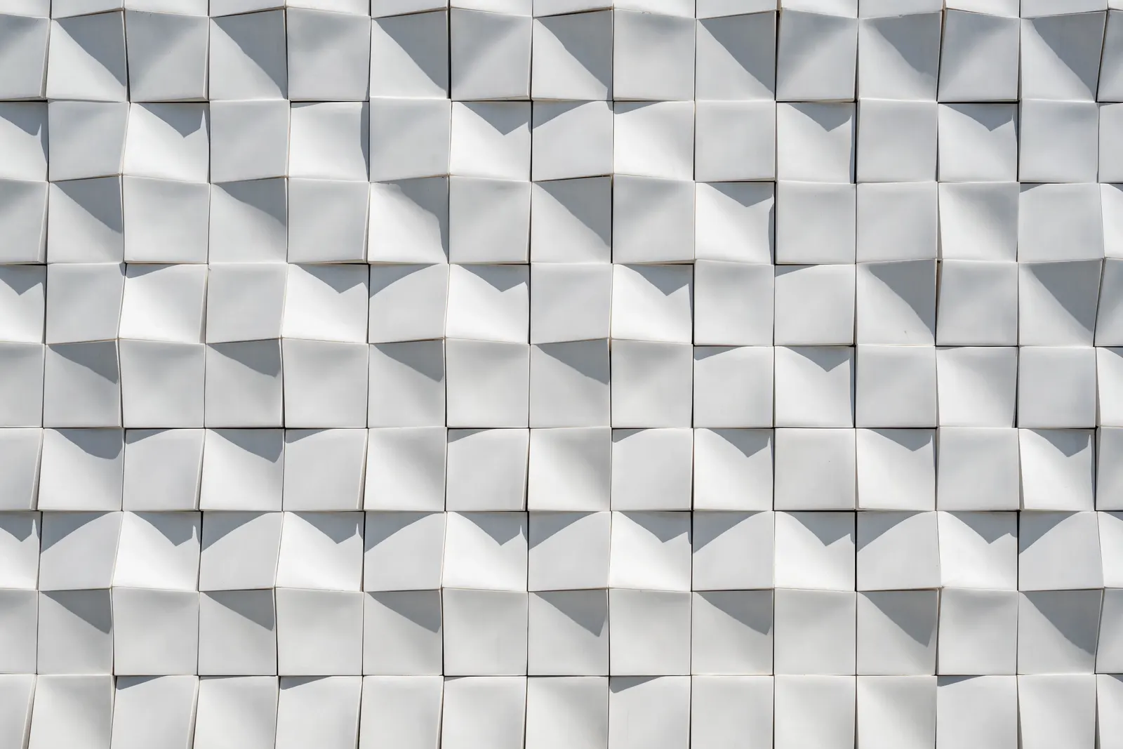 The ceramic facade of DATUM TOWER in close view — matte white facets turning the light into a shallow relief.