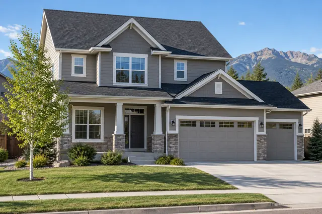 A two-story home with a new charcoal shingle roof and white gutters on a clear morning