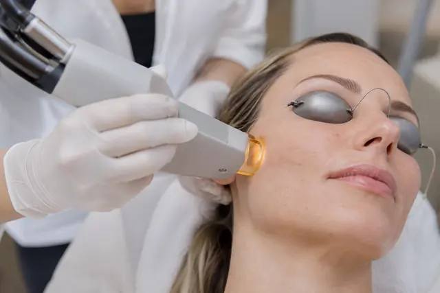 A provider's gloved hands treating a client's cheek in a clean, warmly lit treatment room